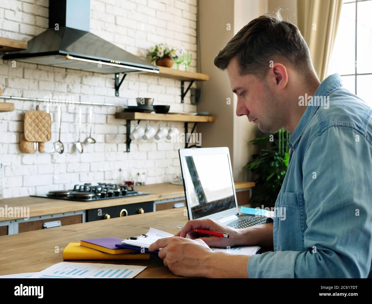 Konzept „Work from Home“. Ein junger Mann arbeitet mit Dokumenten in der Küche. Stockfoto