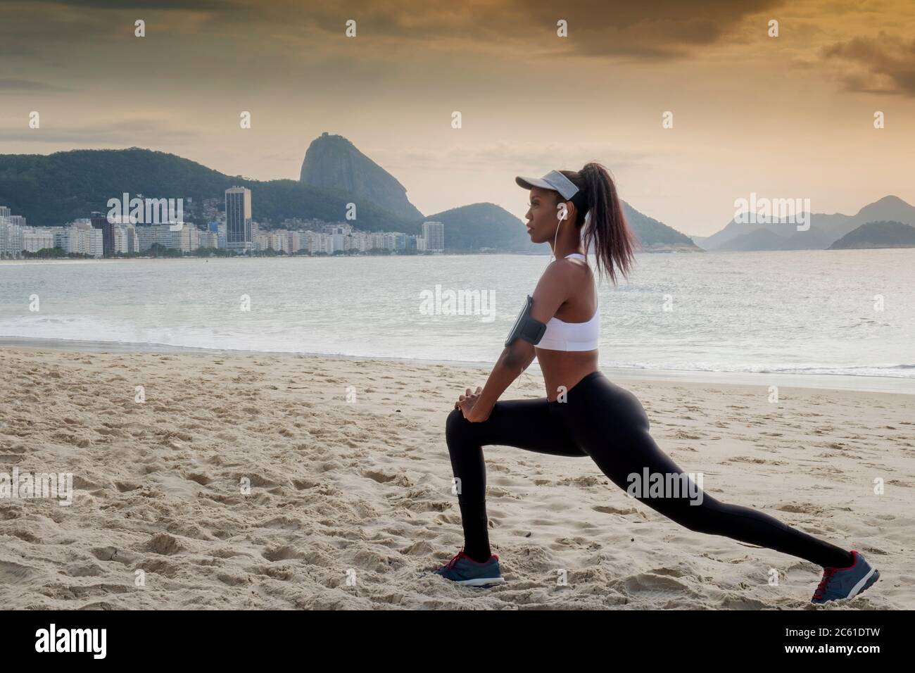 Südamerika, Brasilien, Copacabana Beach. Eine schwarze Brasilianerin in den frühen Dreißigern, die sich vor einem Lauf dehnt Stockfoto