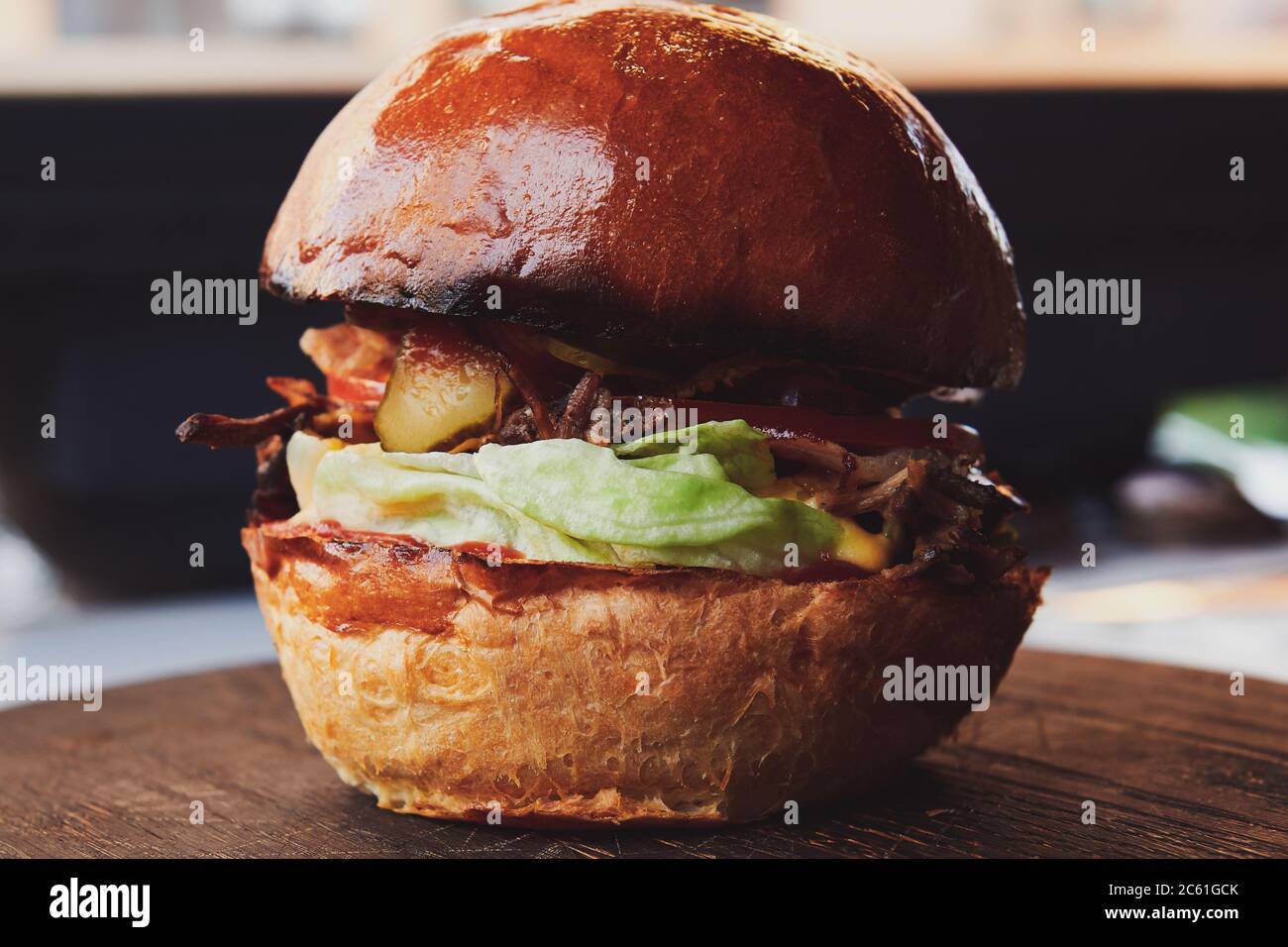 Burger mit Entenfleisch auf dem Holzbrett im Restaurant. Frisches Brötchen mit Salat und eingelegter Gurke. Nahaufnahme. Stockfoto