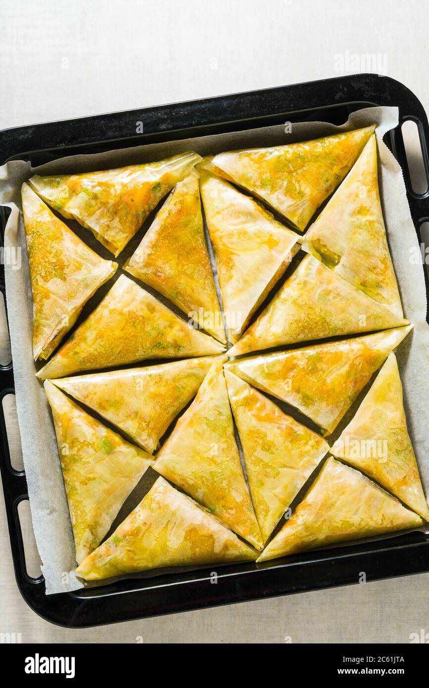 indische Samosa aus Phyllo mit würzigen Kartoffeln und Gemüse auf einem Backblech, fertig zum Backen im Ofen mit schwarzen Sesamsamen Stockfoto