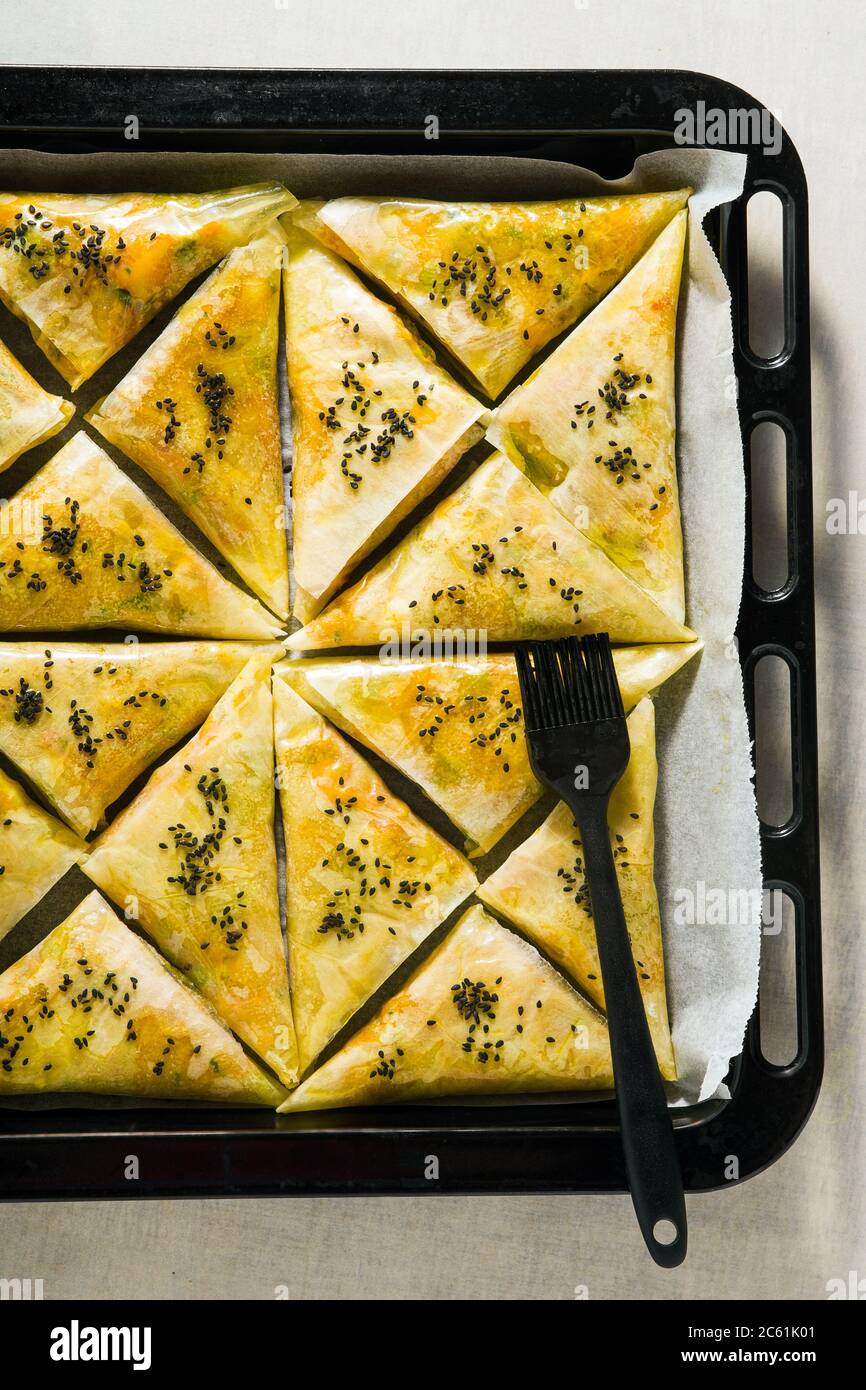 indische Samosa aus Phyllo mit würzigen Kartoffeln und Gemüse auf einem Backblech, fertig zum Backen im Ofen mit schwarzen Sesamsamen Stockfoto