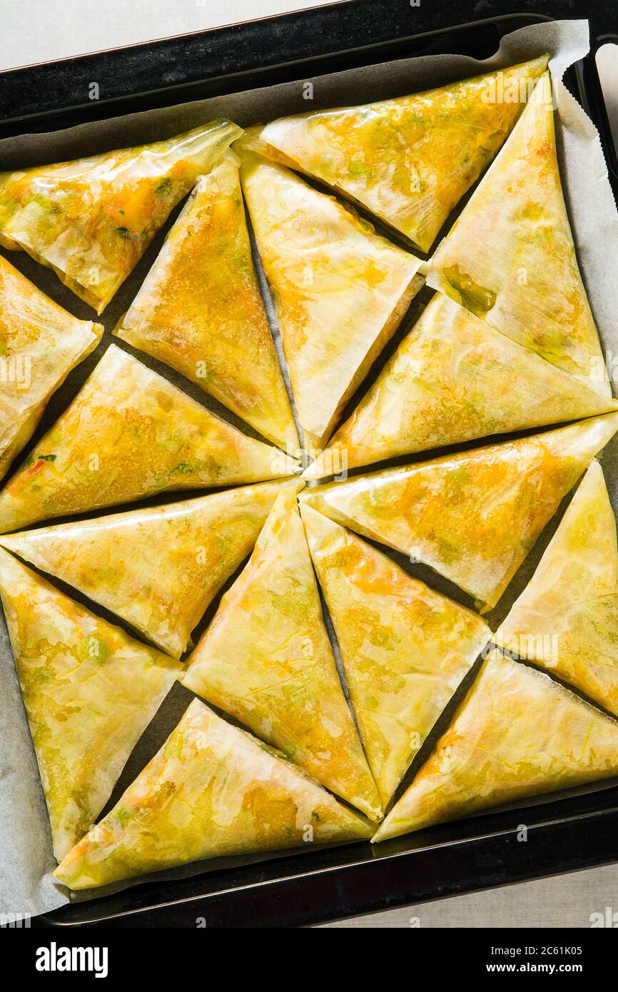 indische Samosa aus Phyllo mit würzigen Kartoffeln und Gemüse auf einem Backblech, fertig zum Backen im Ofen mit schwarzen Sesamsamen Stockfoto