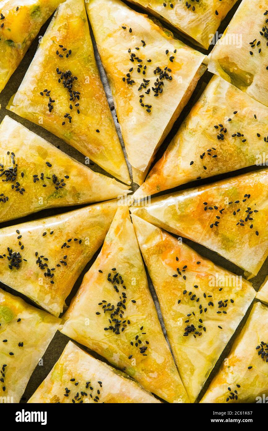 indische Samosa aus Phyllo mit würzigen Kartoffeln und Gemüse auf einem Backblech, fertig zum Backen im Ofen mit schwarzen Sesamsamen Stockfoto