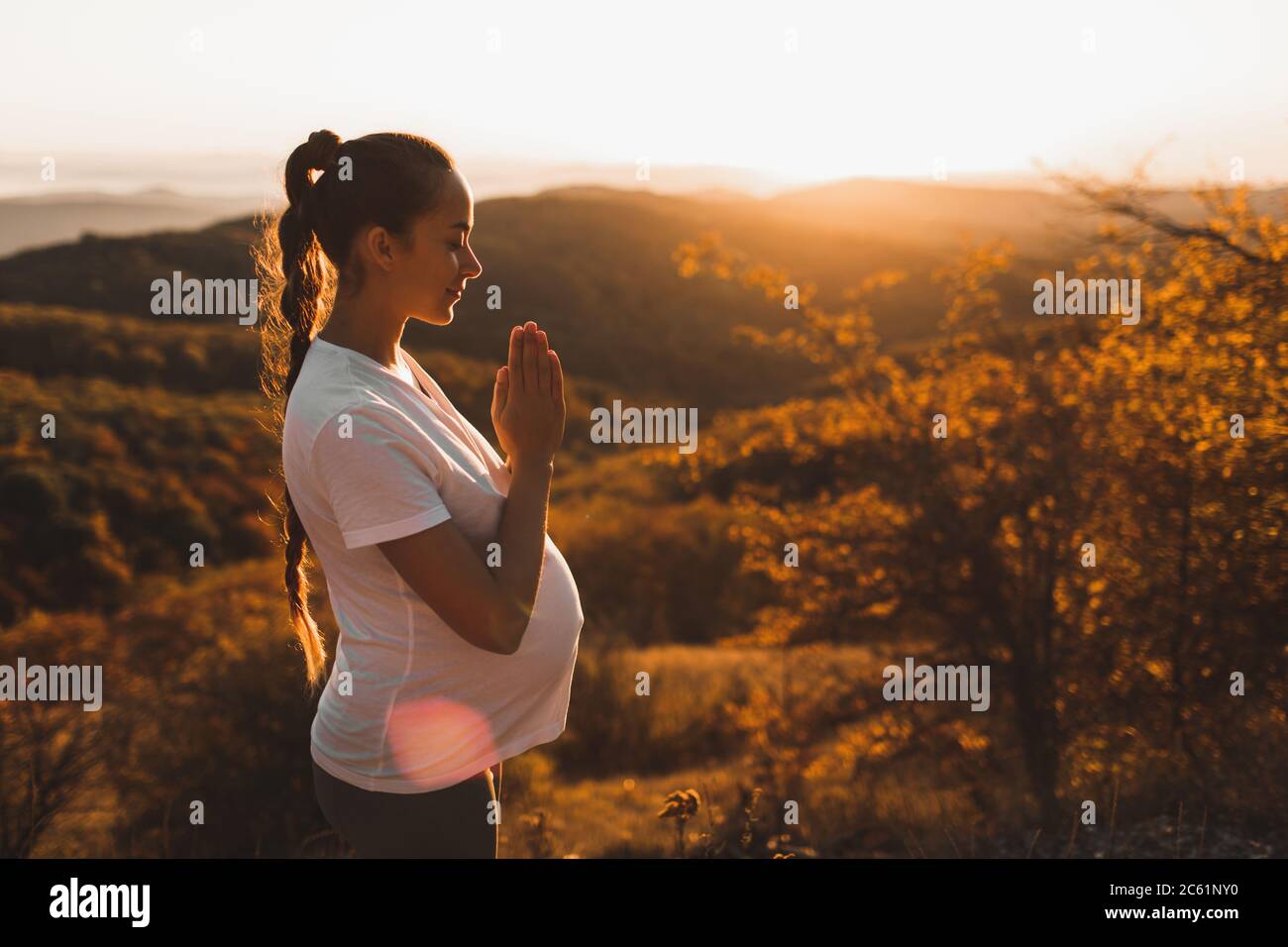 Spirituelles und emotionales Konzept der Harmonie mit der Natur in der Mutterschaft. Schwangere Frau, die Yoga im Freien auf dem Hügel bei Sonnenuntergang praktiziert. Toller Ausblick auf die Berge im Herbst. Stockfoto