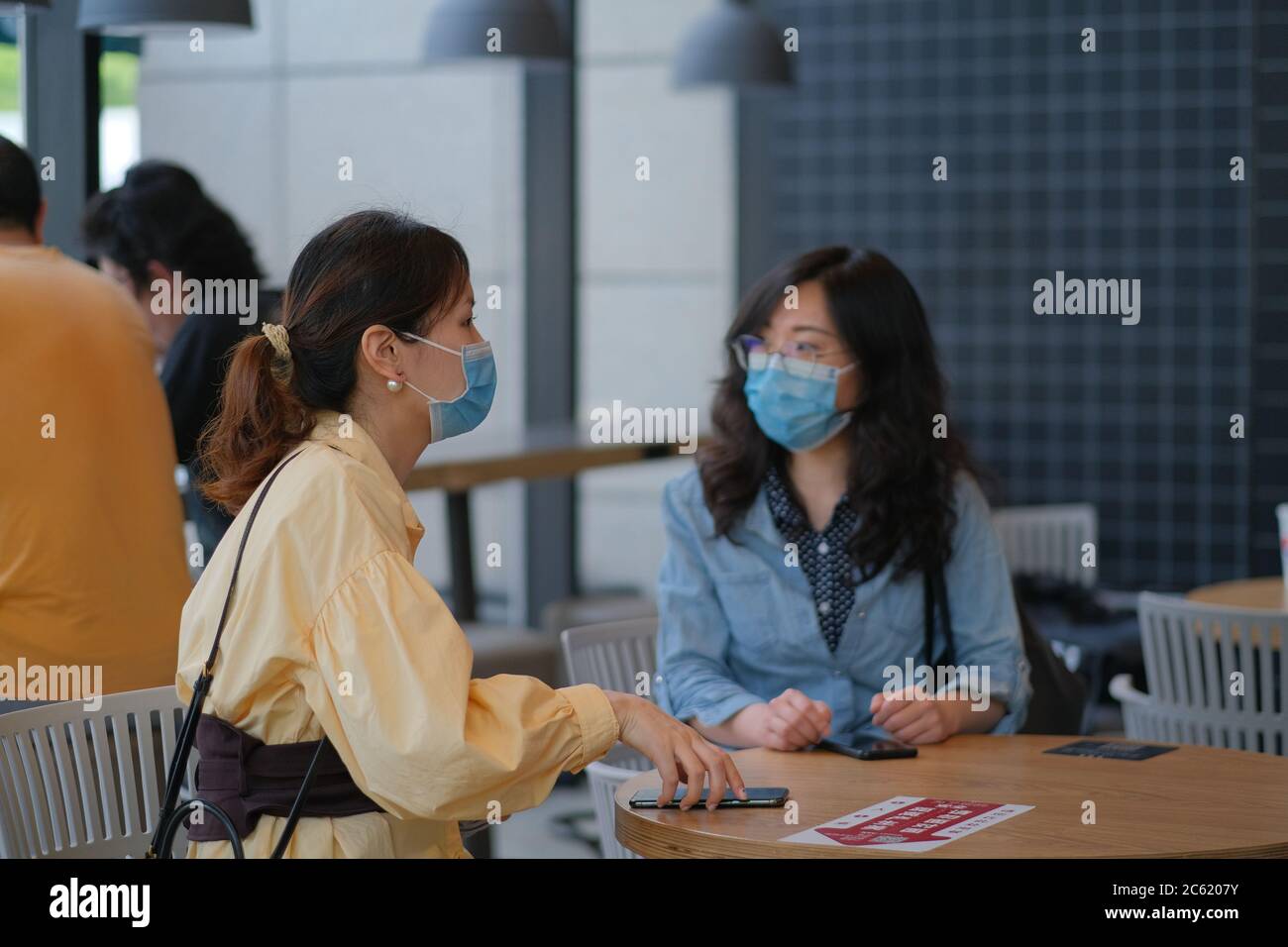 Junge Frauen im Café sprechen, tragen chirurgische Maske, um Infektion von Coronavirus COVID-19 Lungenentzündung zu verhindern Stockfoto
