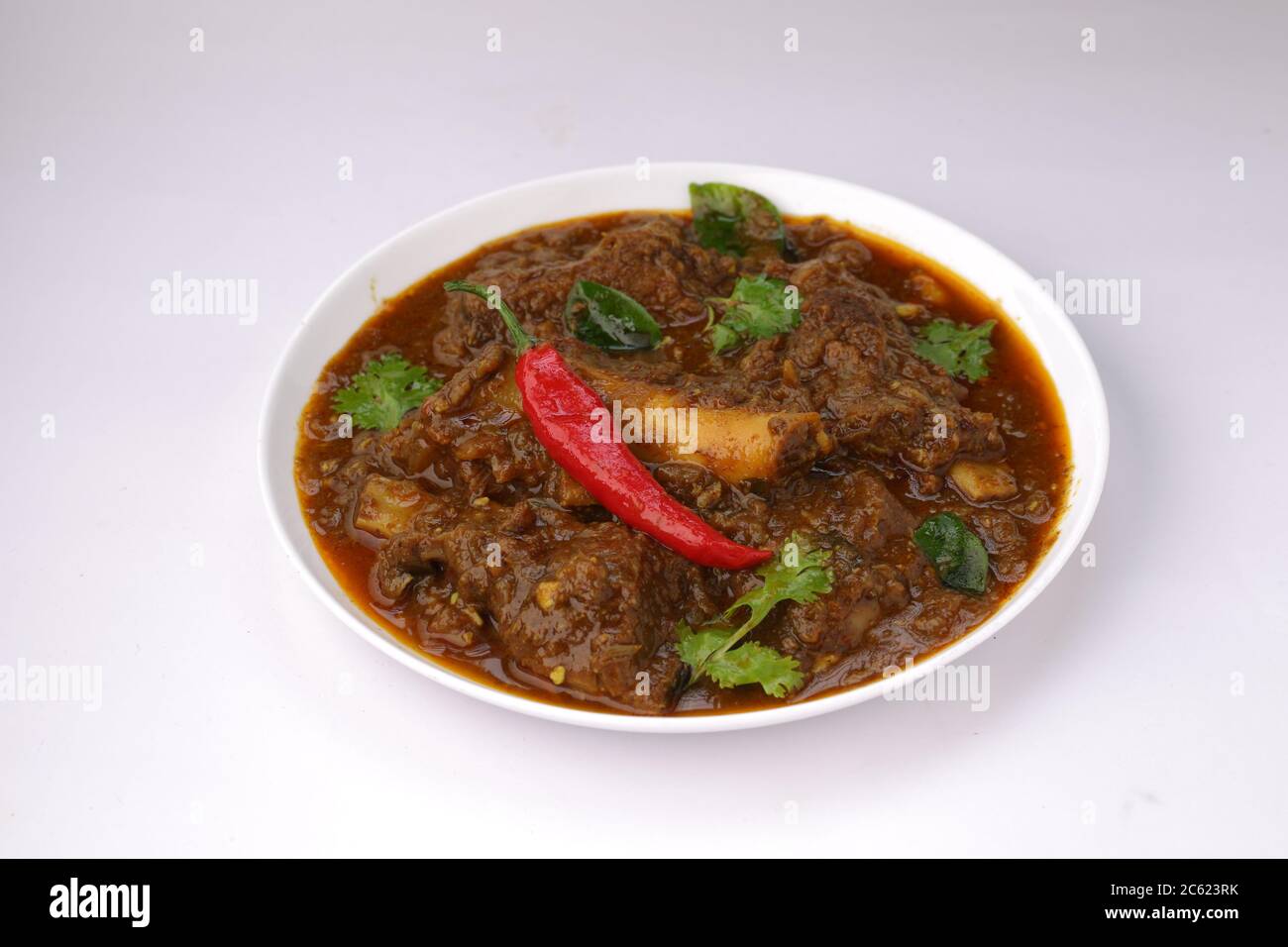 Hammelcurry oder Lamm Curry, würzige und köstliche Gericht garniert mit Curryblättern, Korianderblatt und rote Chili in einem weißen Teller mit weißer Textur oder Stockfoto