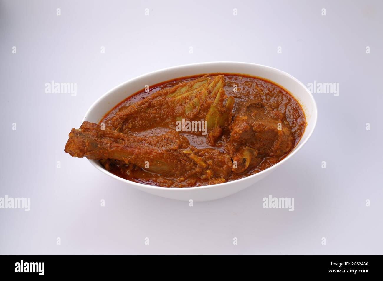Hammelcurry oder Lammcurry, würziges und köstliches Gericht arrangiert Eine weiße ovale Schale mit weißer Textur oder Hintergrund Stockfoto
