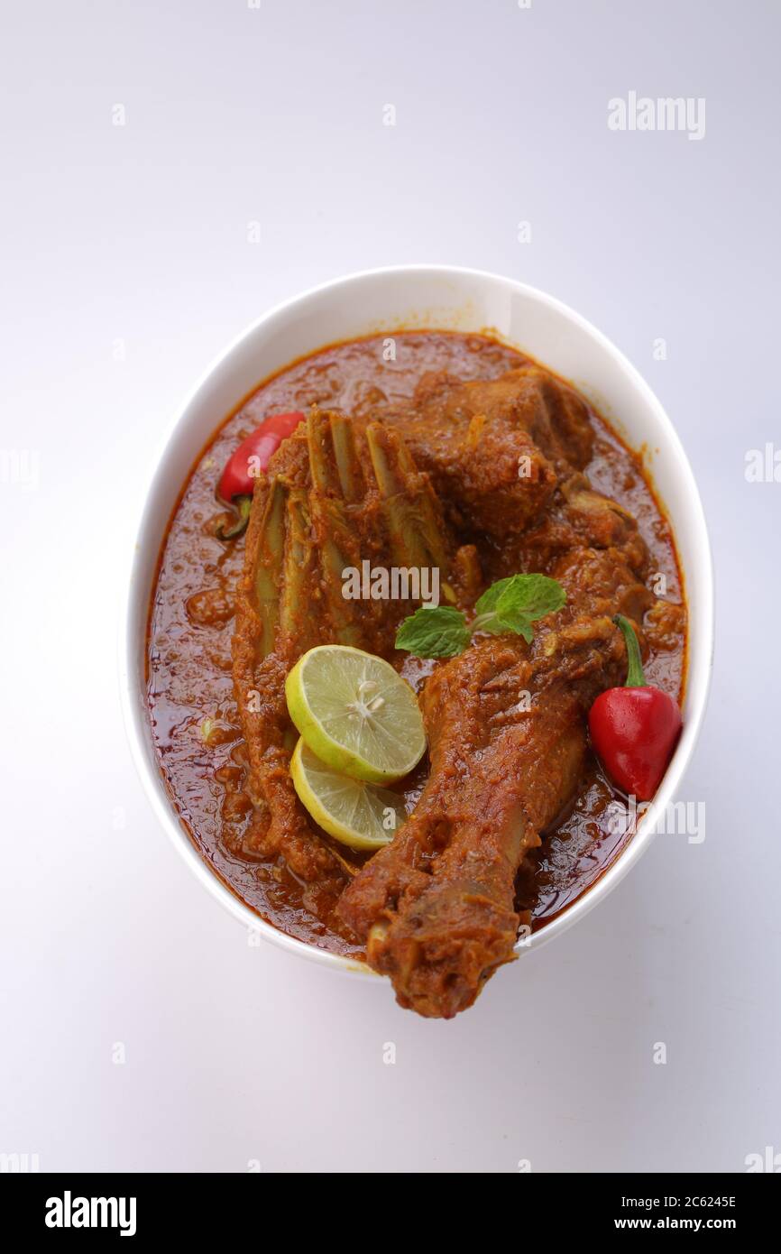 Draufsicht auf Mutton Curry oder Lamm Curry, würziges und leckeres Gericht garniert mit Minzblatt, Zitronenscheiben und rotem Chili in einer weißen ovalen Schüssel mit weiß Stockfoto