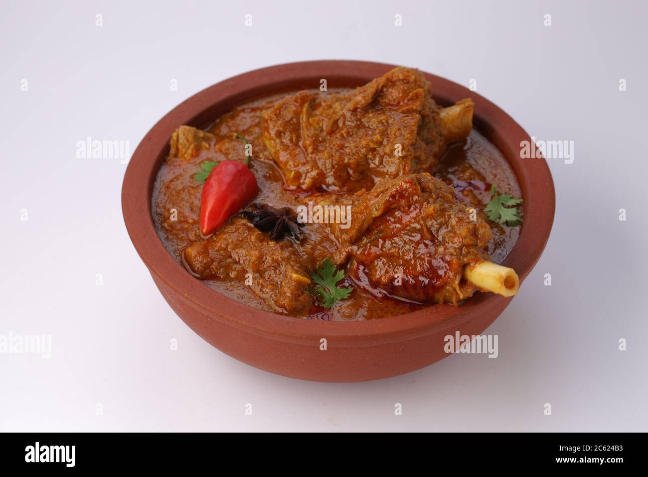 Hammelcurry oder Lammcurry, würziges und köstliches Gericht garniert mit Korianderblatt, roter Chili und Sternanis in einer Steingutschüssel mit Weiß Stockfoto