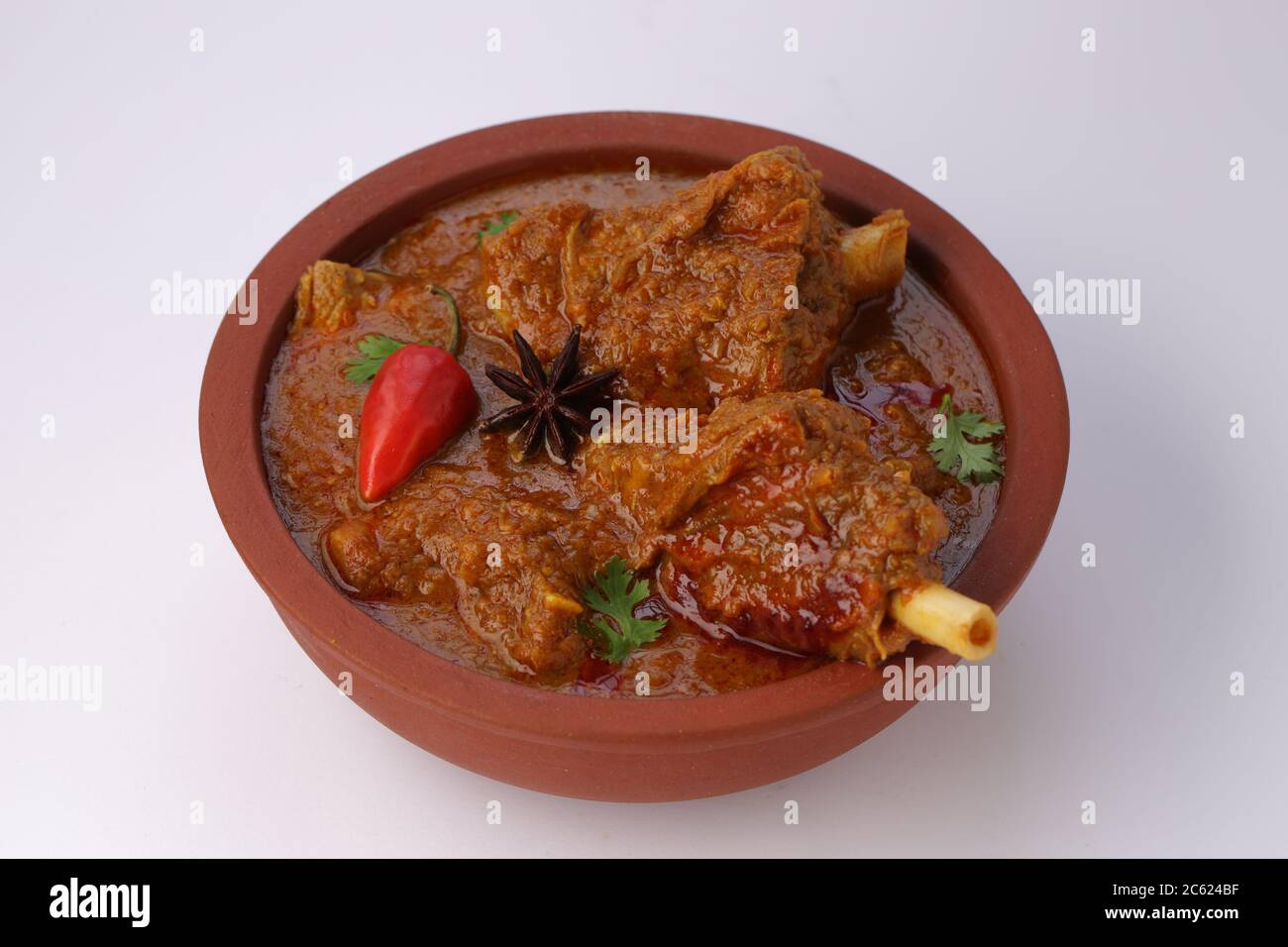 Hammelcurry oder Lammcurry, würziges und köstliches Gericht garniert mit Korianderblatt, roter Chili und Sternanis in einer Steingutschüssel mit Weiß Stockfoto
