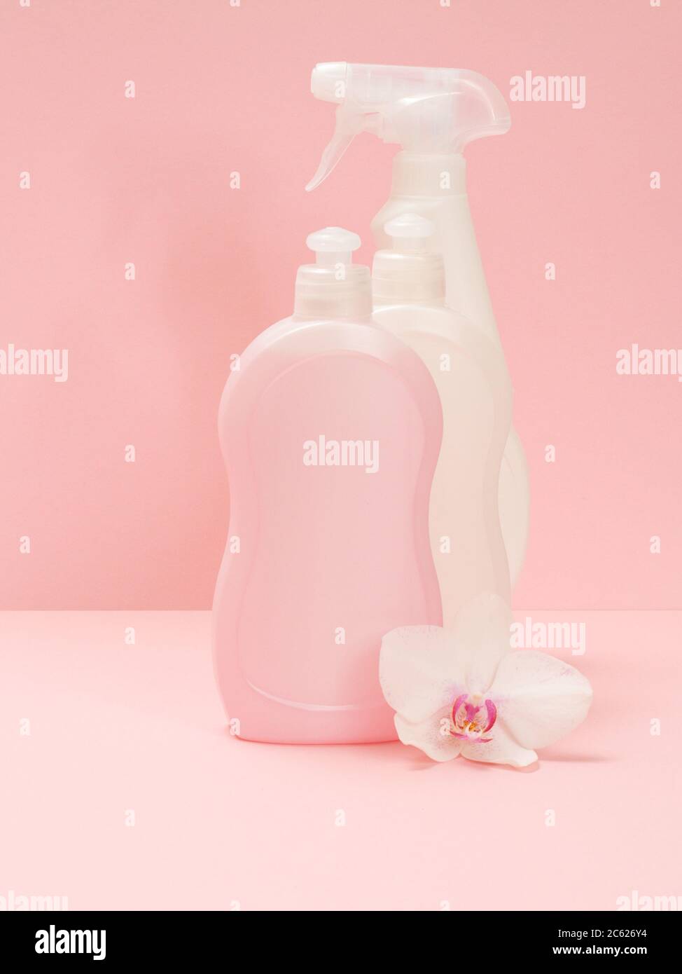Plastikflaschen mit Spülmittel, Glas- und Fliesenreiniger und einer weißen Orchideenblume auf einem rosa Hintergrund. Wasch- und Reinigungsset. Stockfoto