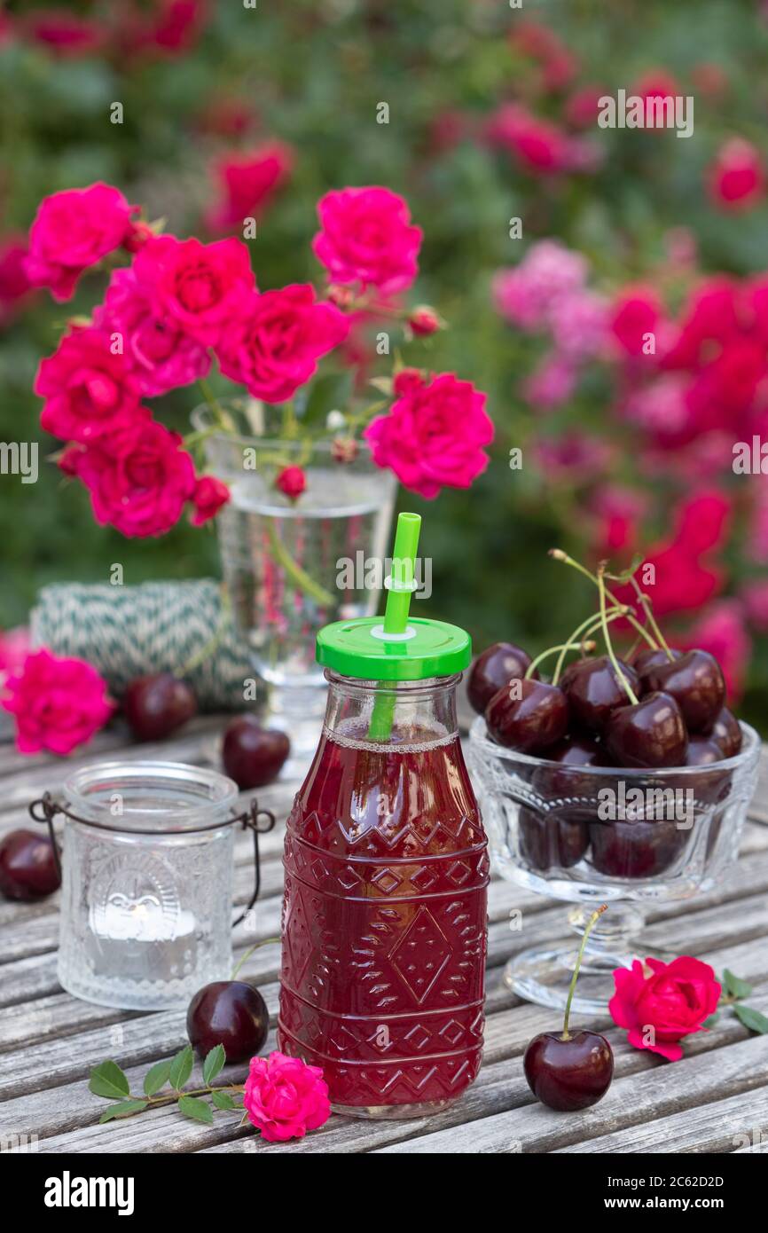 Tischdekoration mit Saftflasche, süßen Kirschen und rosa Rosen Stockfoto