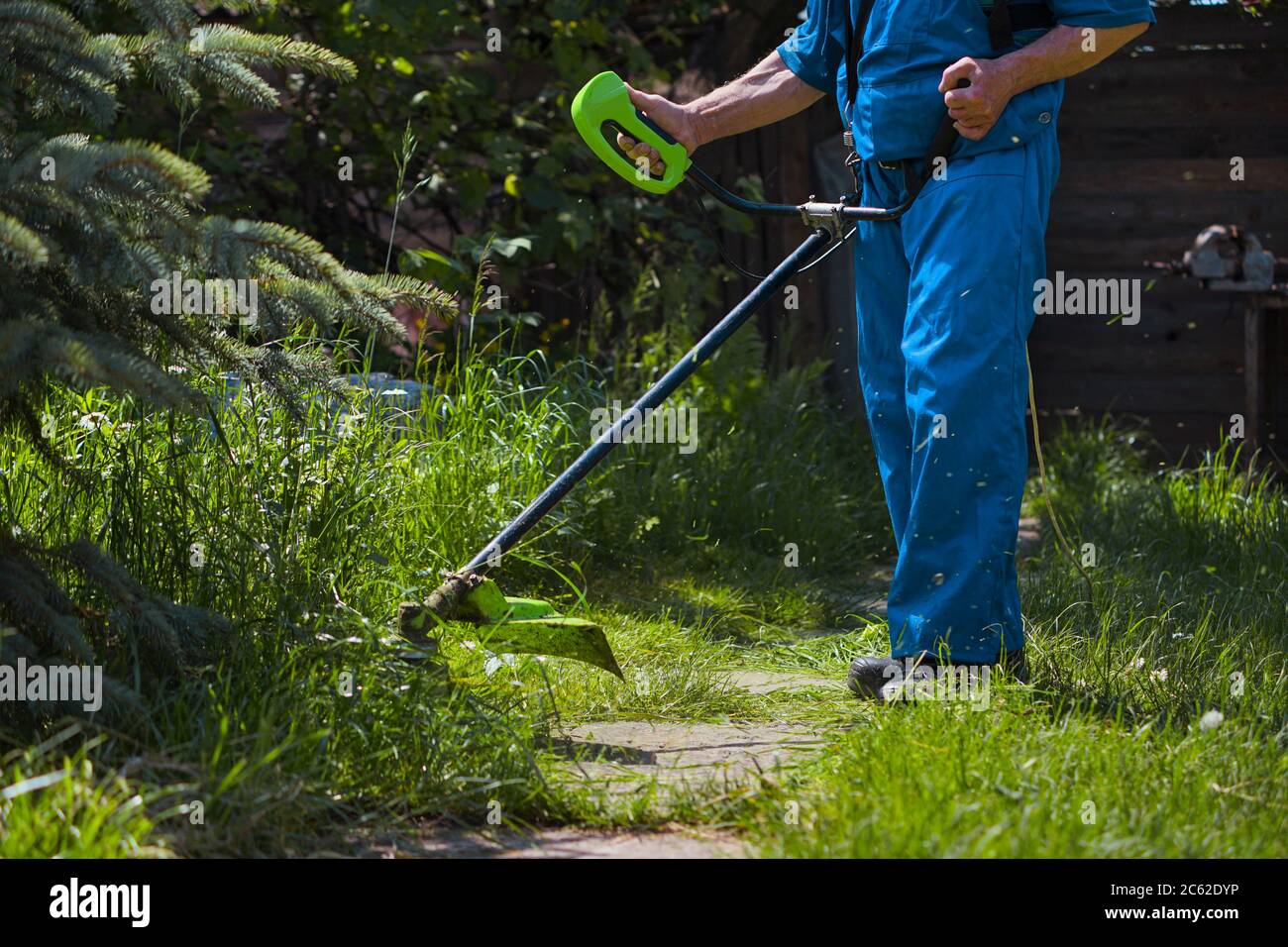 Ein Mann mäht Gras in der Nähe seines Hauses mit einem elektrischen Mäher Stockfoto