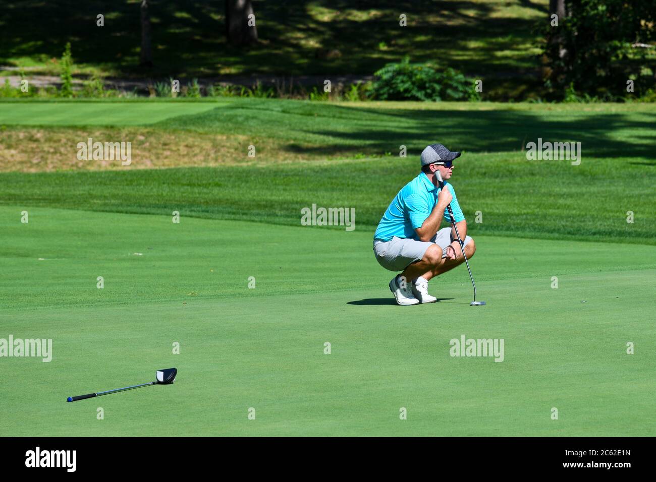 Junger Mann blickt auf einen schönen Golfplatz über das Grün, bevor er seinen Putt Shot nimmt. Stockfoto