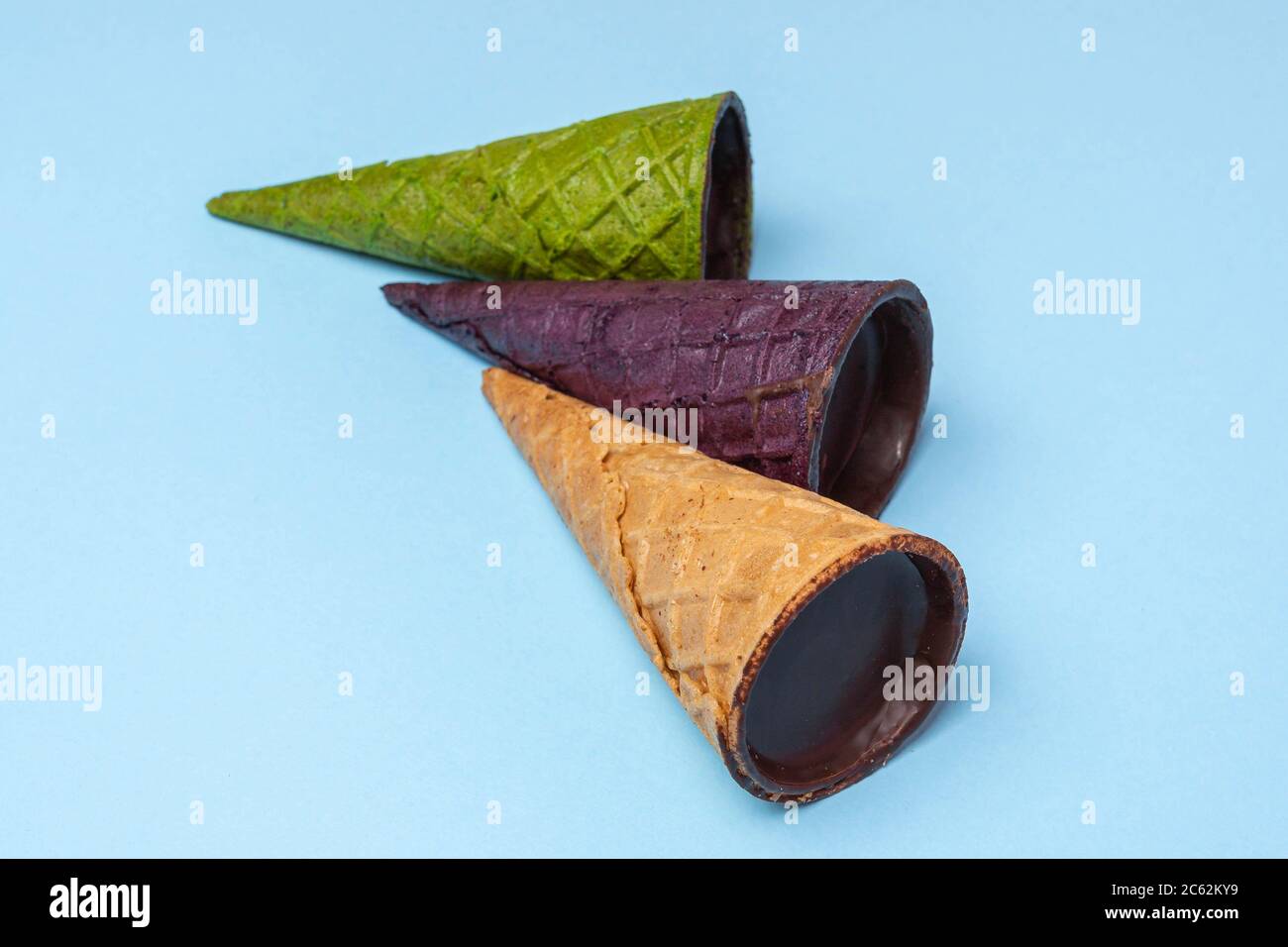 Nahaufnahme von Waffelhörnern gefüllt mit Quark in Schokoladenglasur nebeneinander auf hellblauem Hintergrund platziert, flach legen. Grün, lila, bro Stockfoto