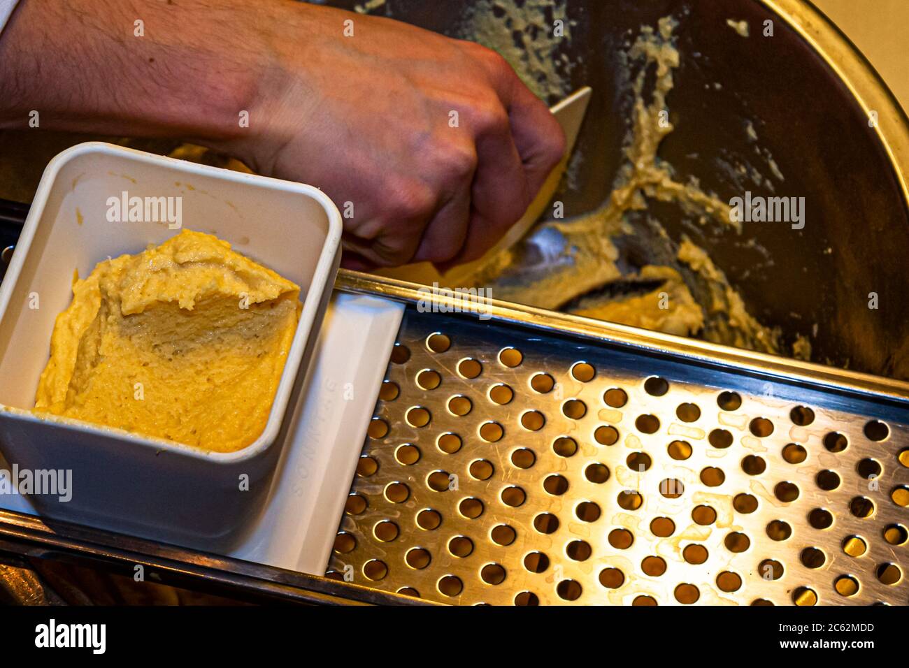 Der Knöpfler in Aktion. Kässpätzler werden auch Käsknöpfle genannt. Frische Pasta mit Reibe - typisch österreichische Käsepasta - Teig fällt in kochendes Wasser Stockfoto