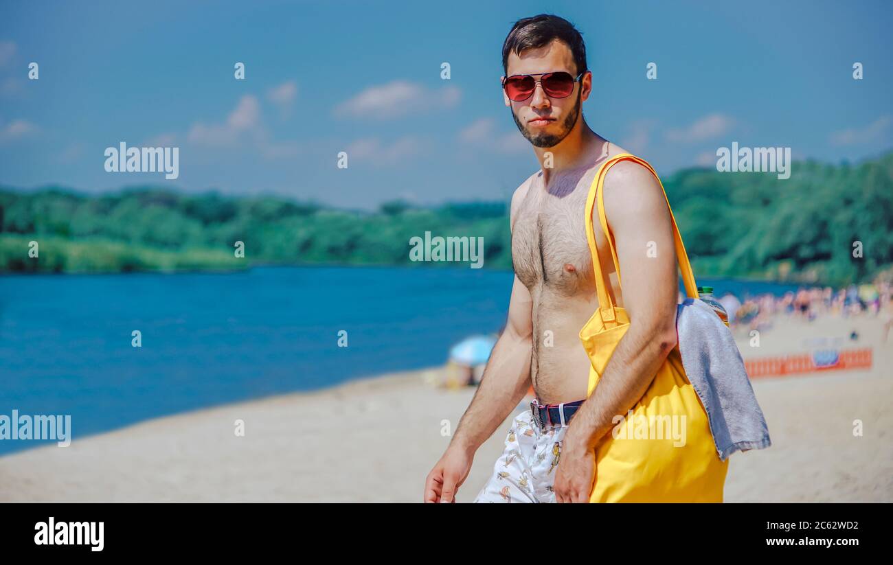 Typ mit gelber Tasche und Sonnenbrille am Strand Stockfoto