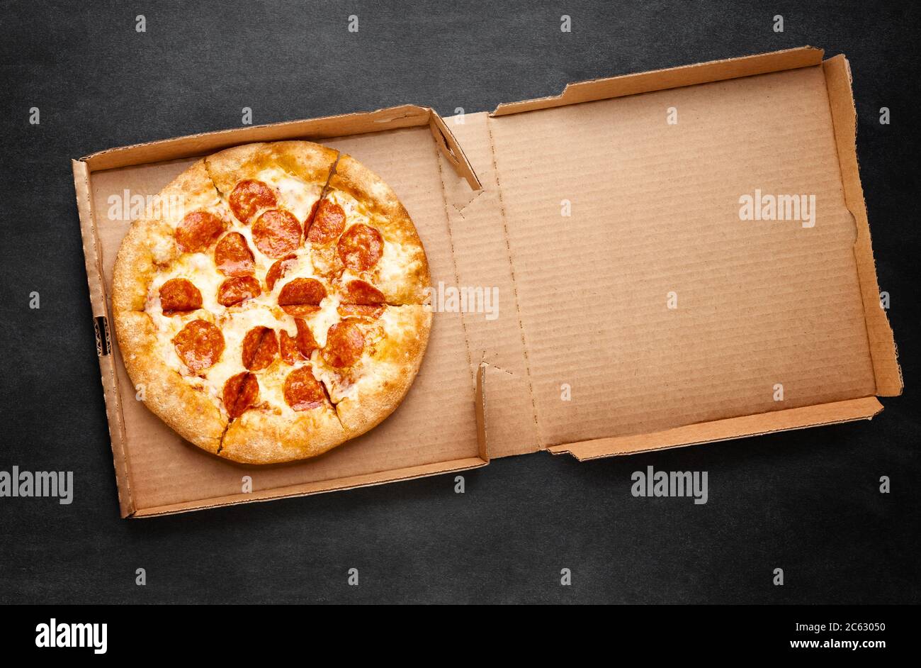 Pizza in einer Pappschachtel auf einer dunklen Tafel. Platz für Ihren Text. Von oben auf das Pizza-Paket. Pizzalieferung. Stockfoto