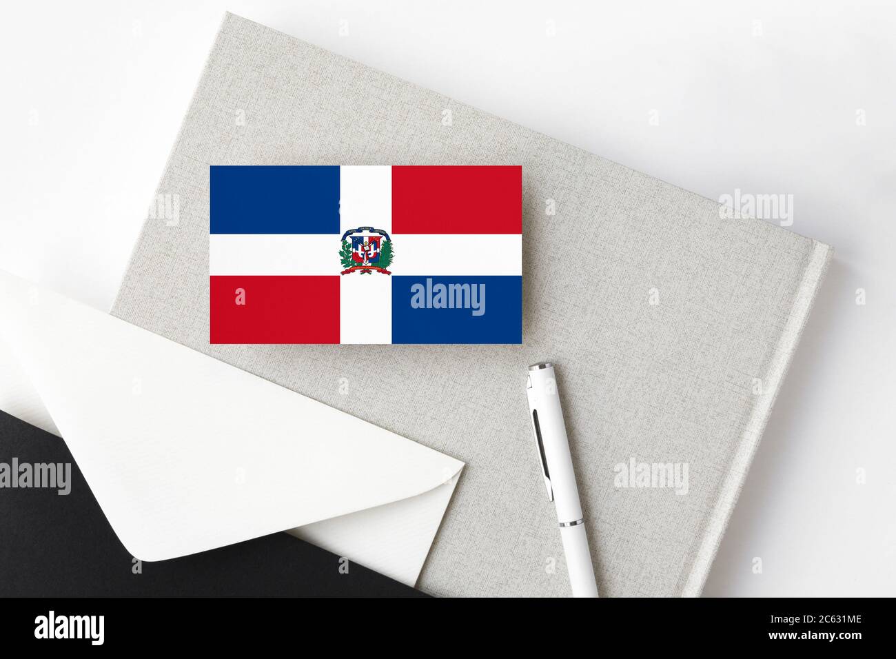 Dominikanische Republik Flagge auf minimalistischen Buchstaben Hintergrund. Nationaler Einladungsumschlag mit weißem Stift und Notizbuch. Kommunikationskonzept. Stockfoto