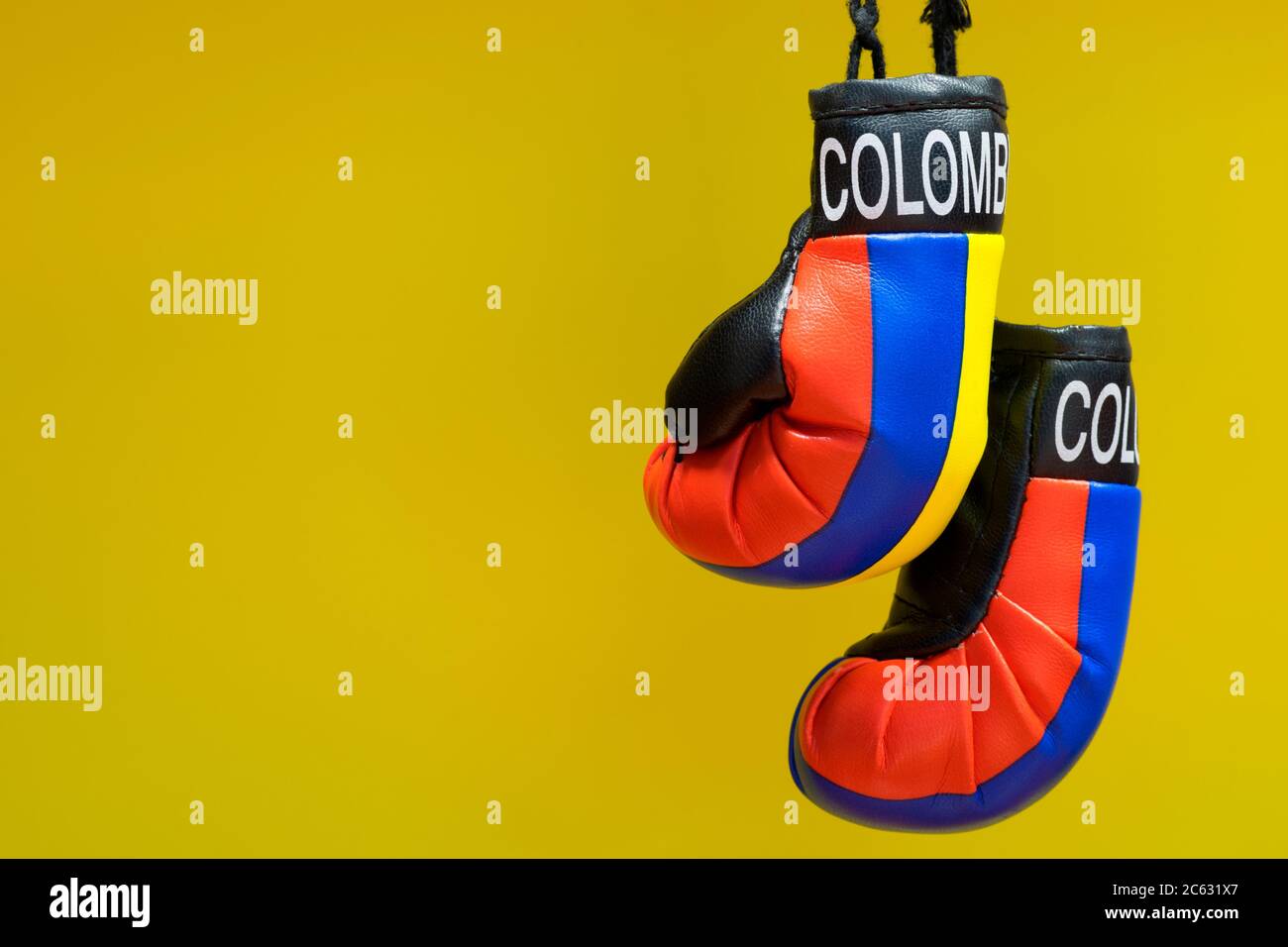 Replica Boxhandschuhe mit Kolumbien Label und Country Farben hängen vor einem schlichten gelben Hintergrund. Kampfkonzept mit Kopierraum. Stockfoto