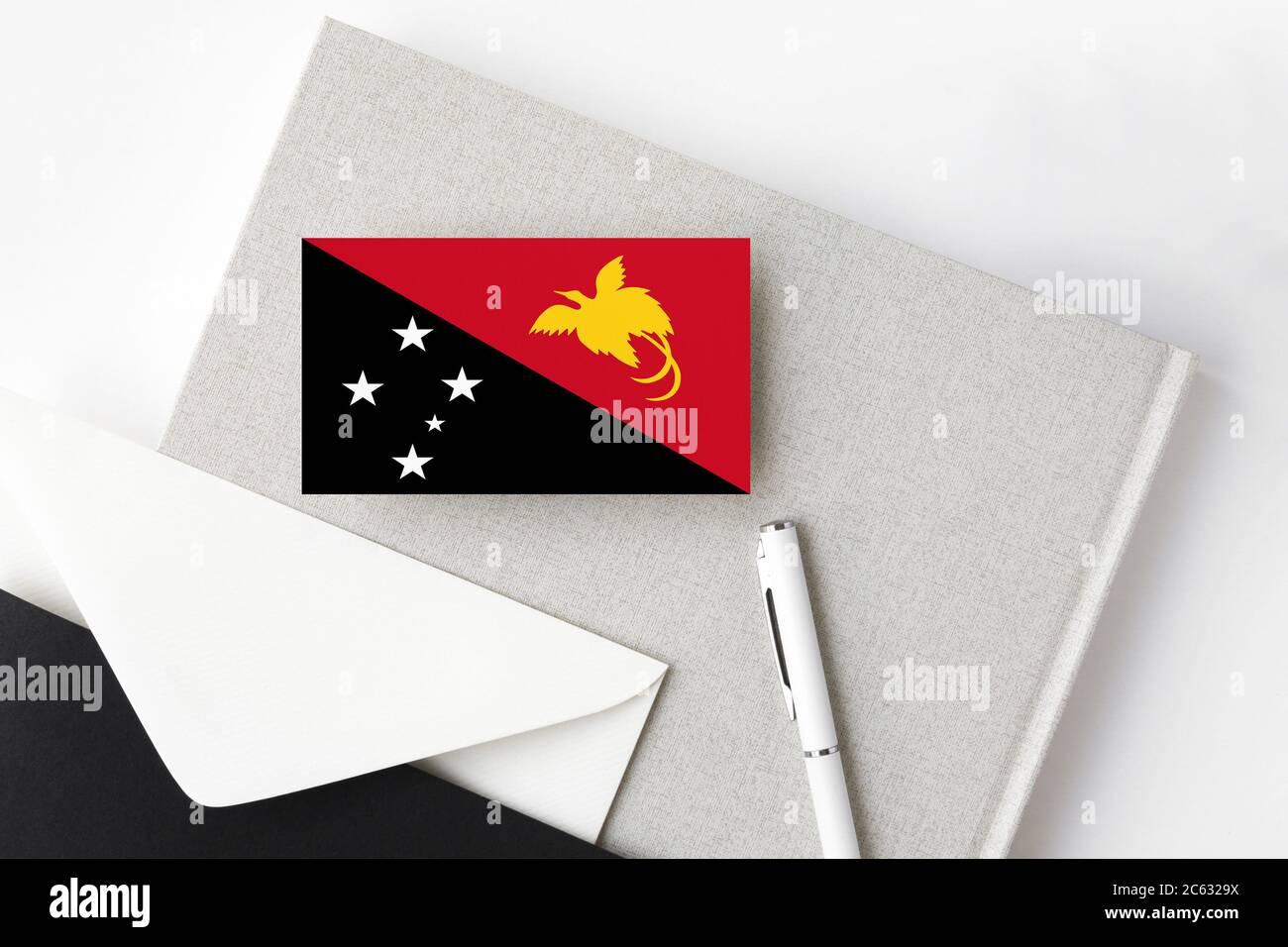 Papua-Neuguinea-Flagge auf minimalistischem Buchstabenhintergrund. Nationaler Einladungsumschlag mit weißem Stift und Notizbuch. Kommunikationskonzept. Stockfoto
