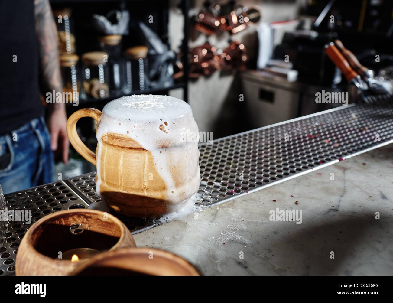Kaltes Craft-Bier in einer Keramikschale mit Schaumtropfen. Ein Barkeeper, der in der Nähe der Theke in einem Pub steht Stockfoto