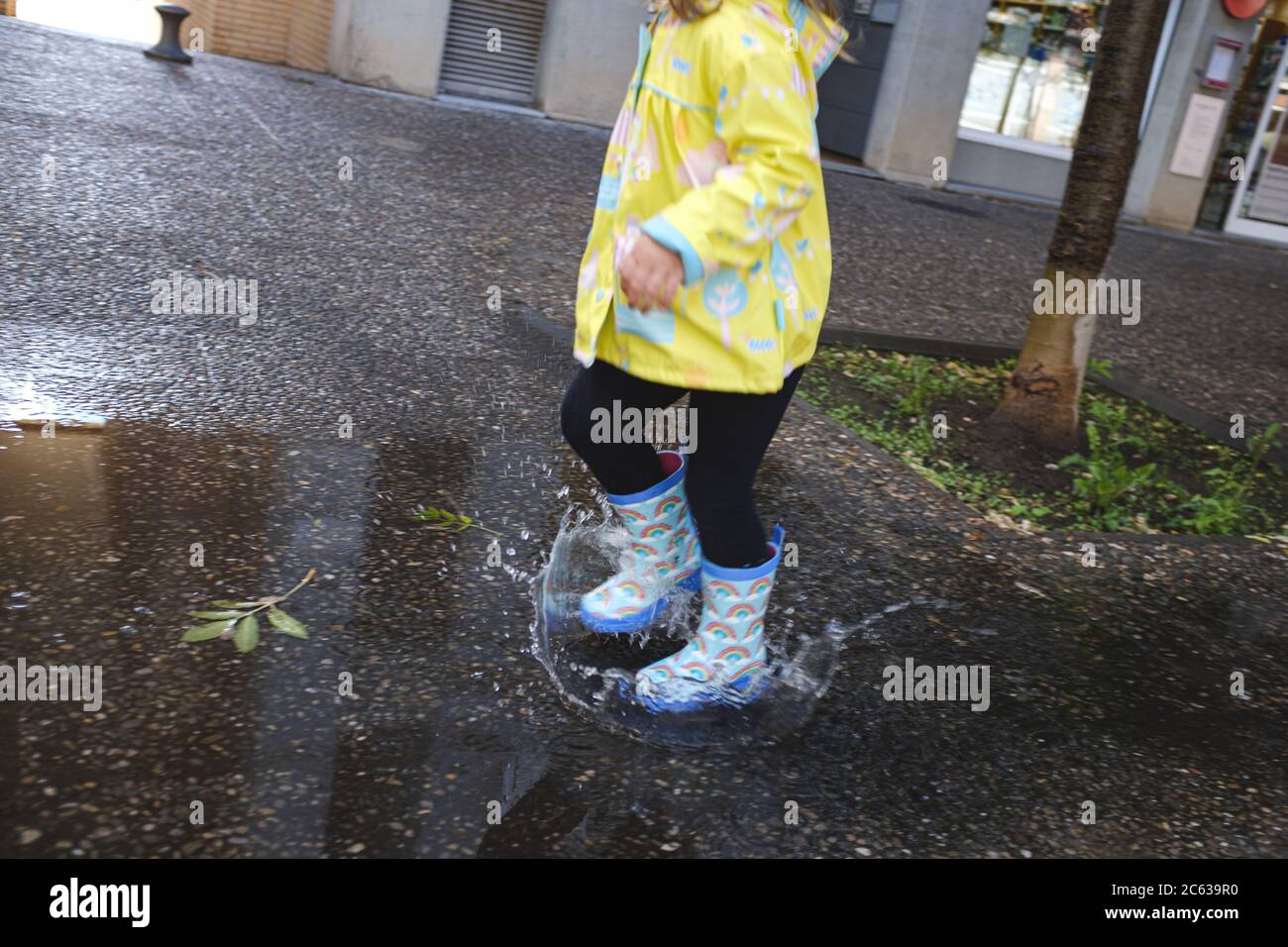 Mädchen spielt auf einer städtischen Szene springen über Wasserpfützen mit blauen Regenbogenstiefel Stockfoto