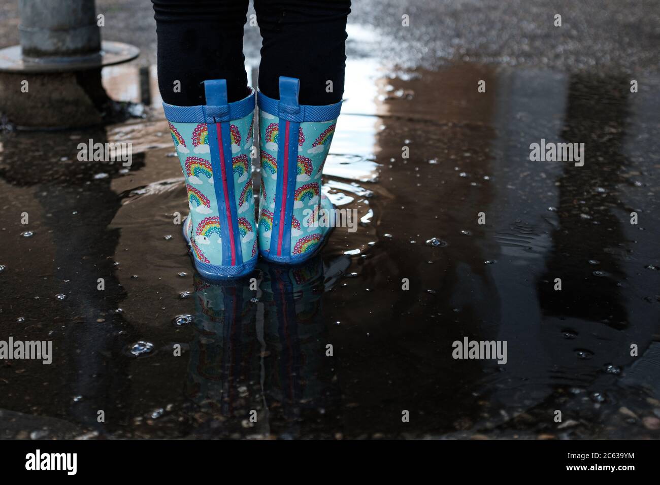 Mädchen spielt auf einer städtischen Szene springen über Wasserpfützen mit blauen Regenbogenstiefel Stockfoto