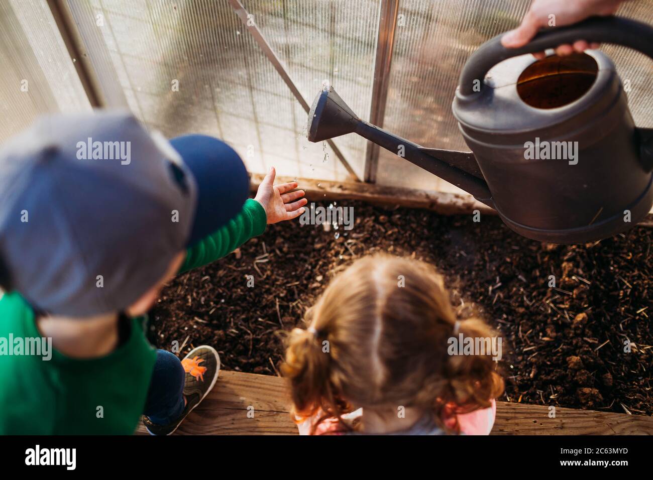 Zwei kleine Kinder helfen Mama Wasserpflanzen im Garten Gewächshaus Stockfoto