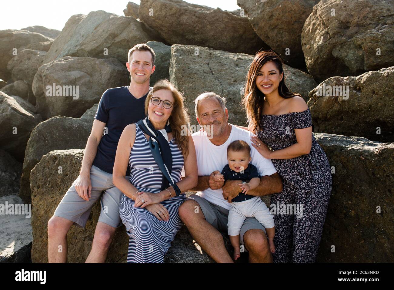 Familie von fünf lächelnd für Kamera sitzend auf Felsen an Strand Stockfoto