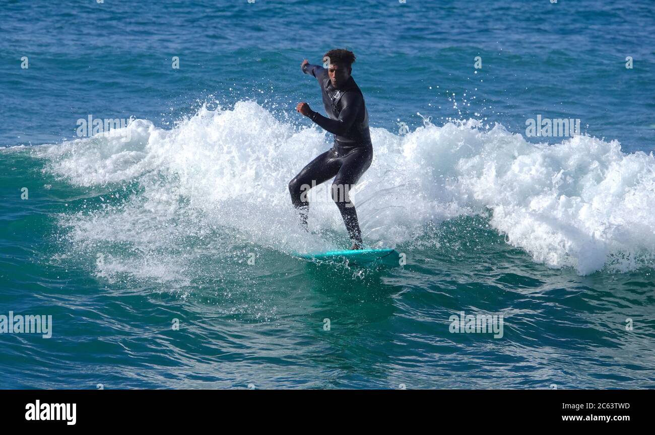 Teenager-Surfer (afroamerikanisch) auf einer Welle auf blauem Brett reiten Stockfoto