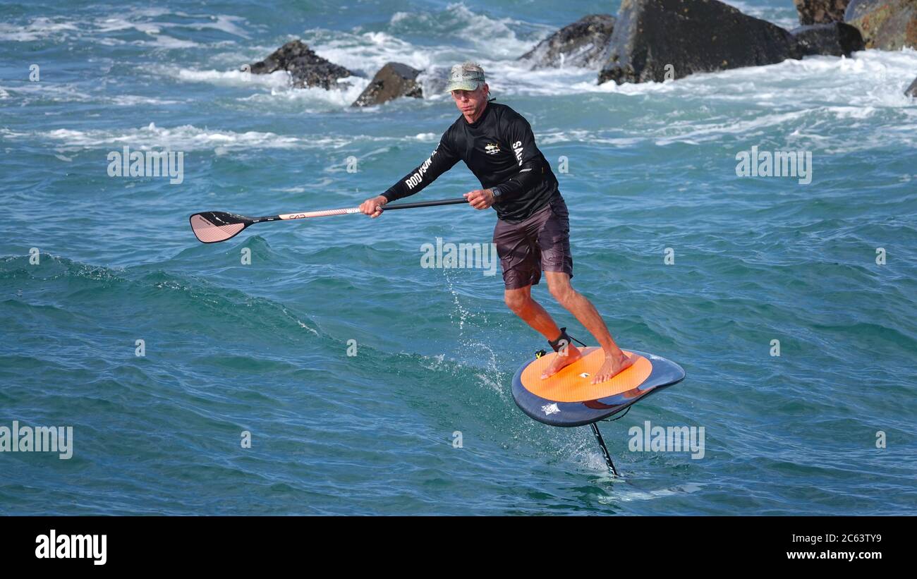 Älterer Mann, der fit bleibt, indem er Spaß auf dem Tragflügelboot hat, steht auf dem Paddle Board Stockfoto