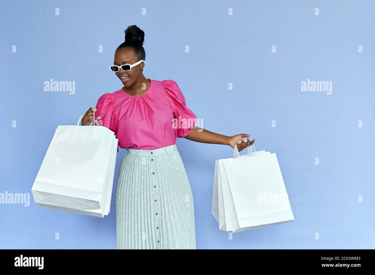 Aufgeregt afrikanische Frau suchen in Einkaufstaschen isoliert auf violett. Stockfoto