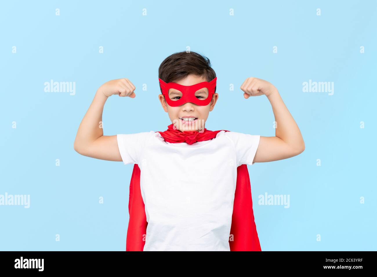 Cute Superhelden Jungen in roten Maske und Umhang biegenden Arm Muskeln isoliert hellblauen Hintergrund Stockfoto