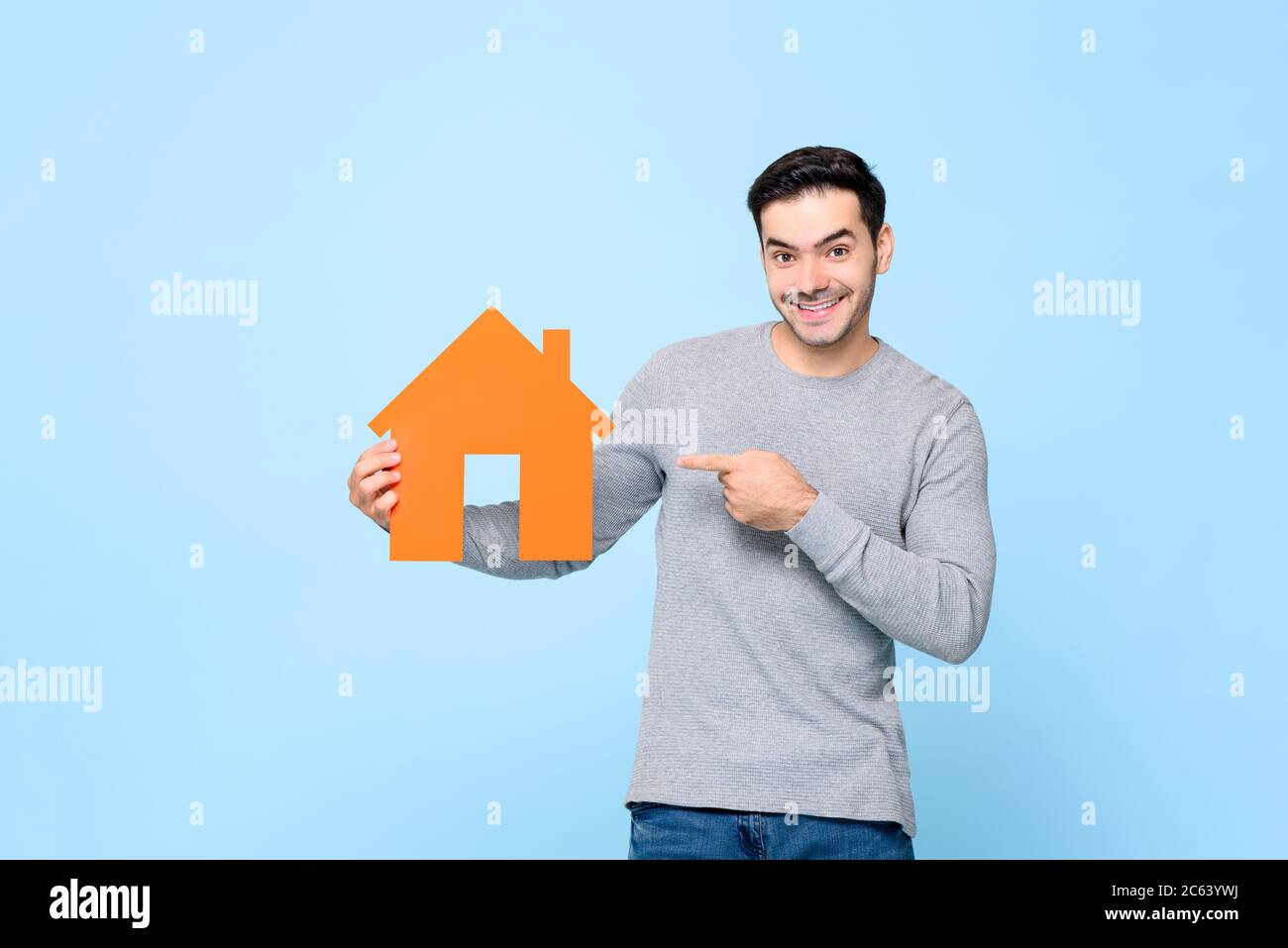 Lächelnder kaukasischer Mann hält und poiting zum Haus Ausschnitt Modell isoliert auf hellblauem Hintergrund Stockfoto