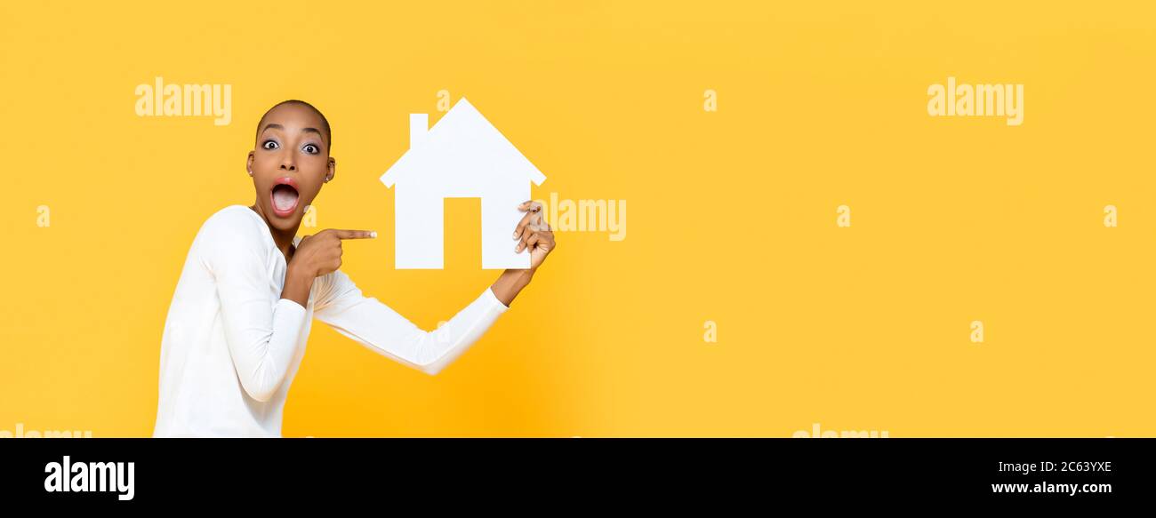 Schockiert afroamerikanische Frau keuchend und zeigt auf Haus Ausschnitt Modell isoliert auf gelben Banner Hintergrund mit Kopieplatz Stockfoto