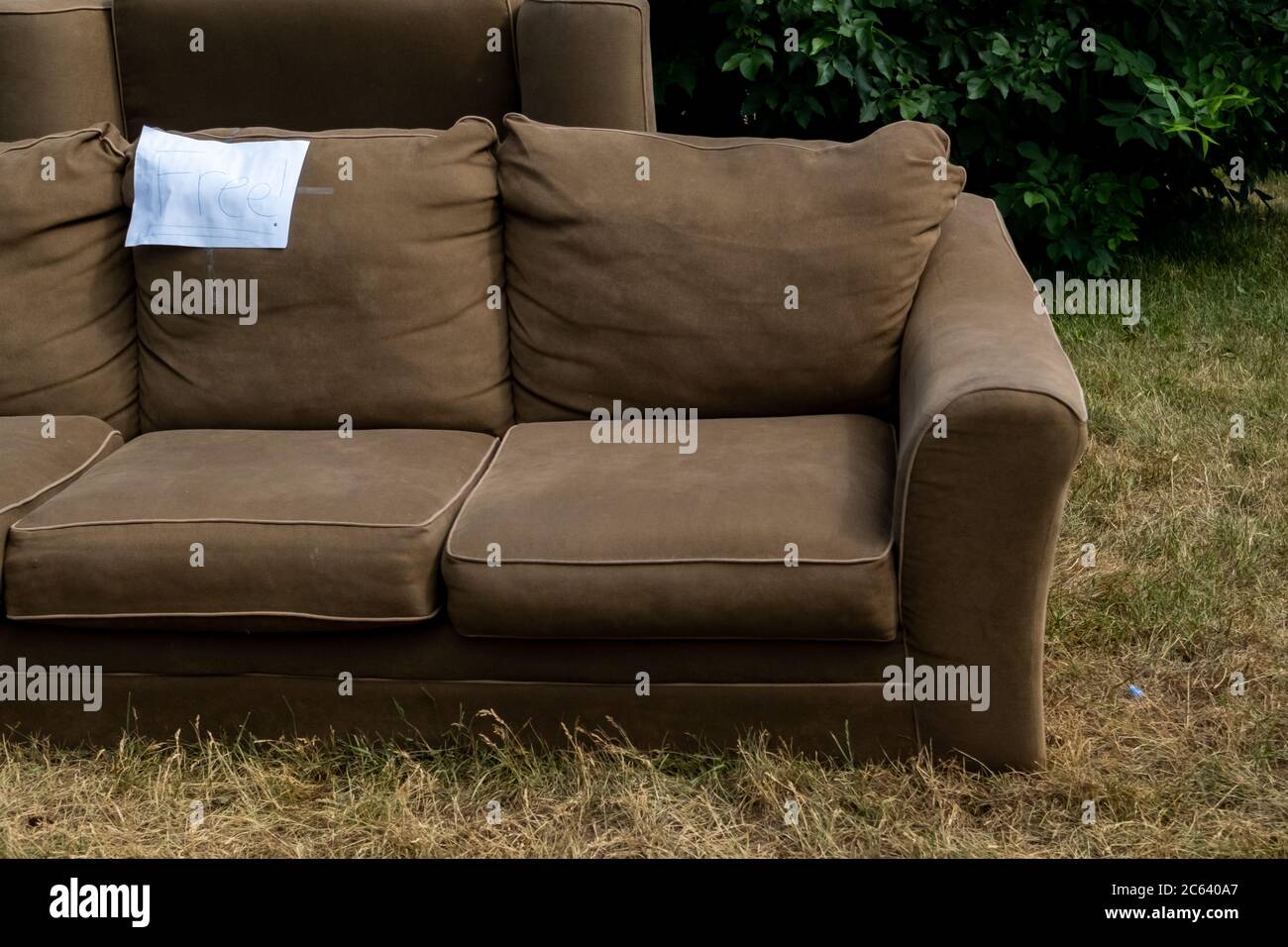 Ein Sofa sitzt auf dem Gras einer vorderen Wiese neben der Straße mit dem Wort "frei" darauf geschrieben. Stockfoto