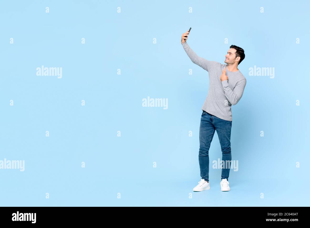 Ganzkörper-Porträt von jungen schönen Mann, der Selfie auf Handy isoliert auf hellblauem Hintergrund mit Kopieplatz Stockfoto