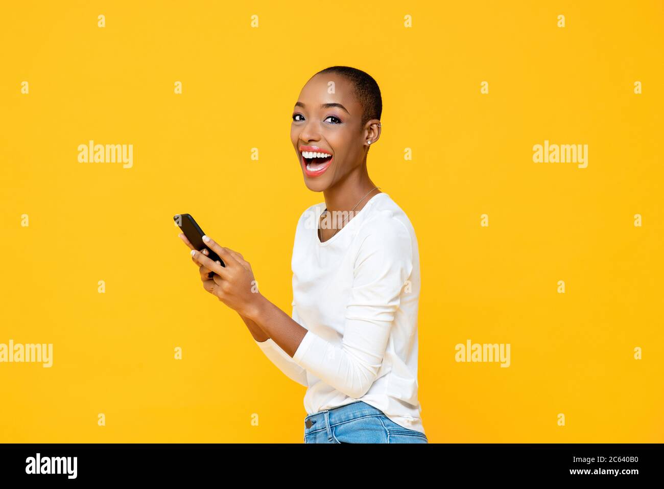 Aufgeregt lächelnde afroamerikanische Frau genießen Anwendung auf Smartphone isoliert auf gelben Studio-Hintergrund Stockfoto