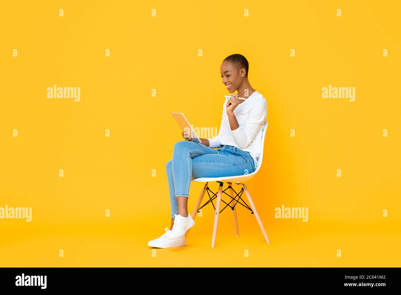 Junge afroamerikanische Frau sitzt und mit Tablet-Computer mit Stift auf isoliertem gelben Hintergrund Stockfoto