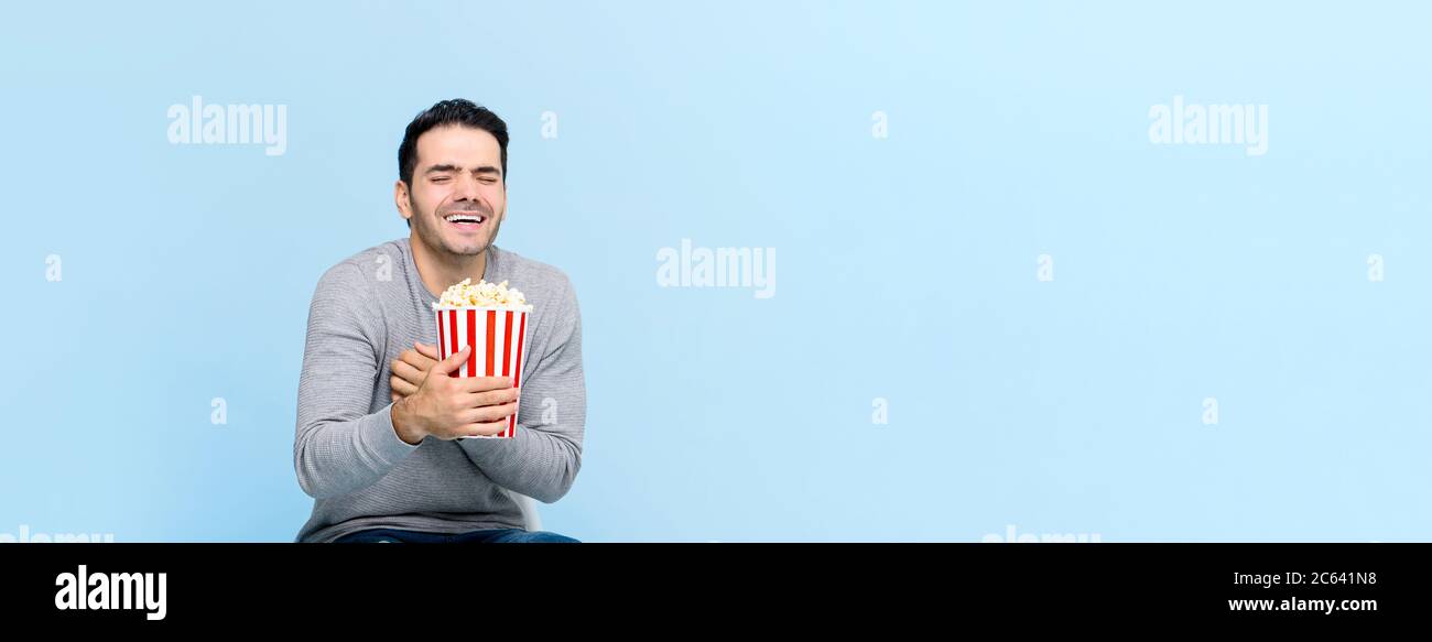 Junger Mann hält Popcorn lachend, während Film isoliert auf hellblauem Banner Hintergrund mit Kopierer Platz Stockfoto