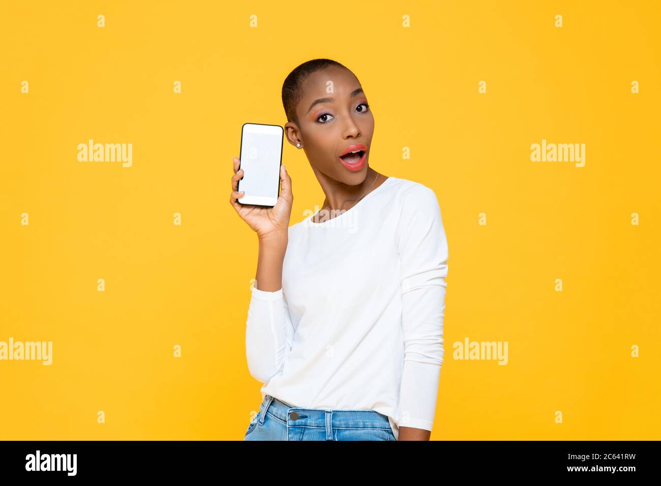 Überrascht schöne afroamerikanische Frau hält Handy mit leerem Bildschirm auf isoliertem gelben Hintergrund Stockfoto