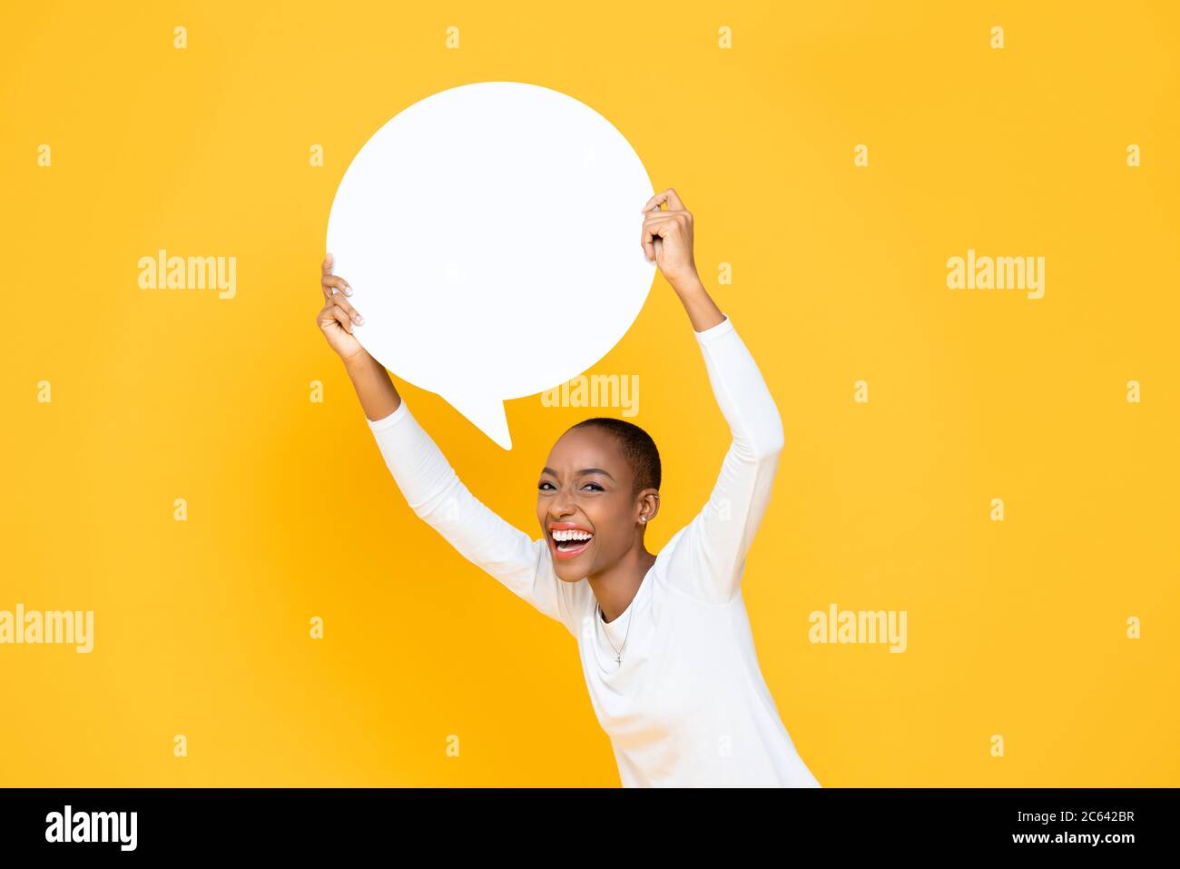 Fröhliche glücklich junge afroamerikanische Frau lächelnd und halten Sprechblase mit leerem Raum für Text über dem Kopf isoliert auf gelbem Hintergrund Stockfoto
