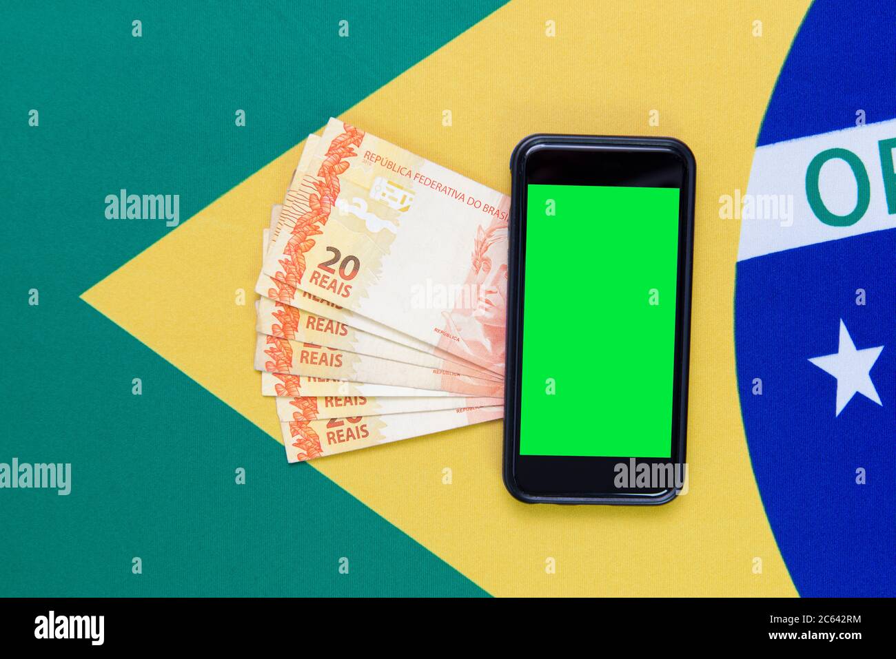 Draufsicht auf brasilianische Green Screen Handy mit Reail Bills über brasilianische Flagge im Hintergrund. Kopieren Sie Leerzeichen und grünen Bildschirm, um Texte und einzufügen Stockfoto