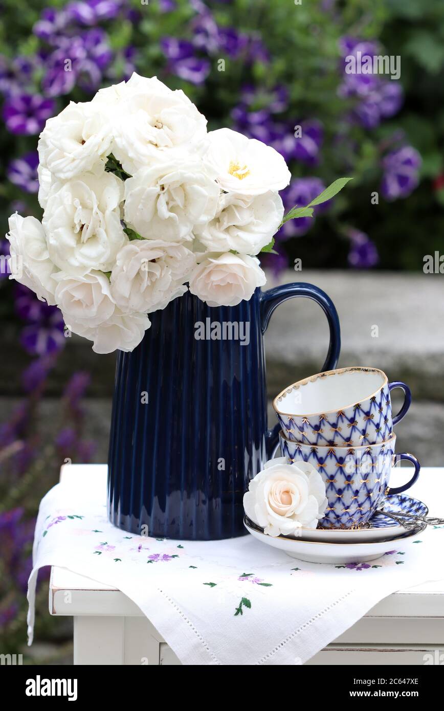 Blumenstrauß aus weißen Rosen in Vase und Vintage Kaffeetassen als Sommerdekoration Stockfoto