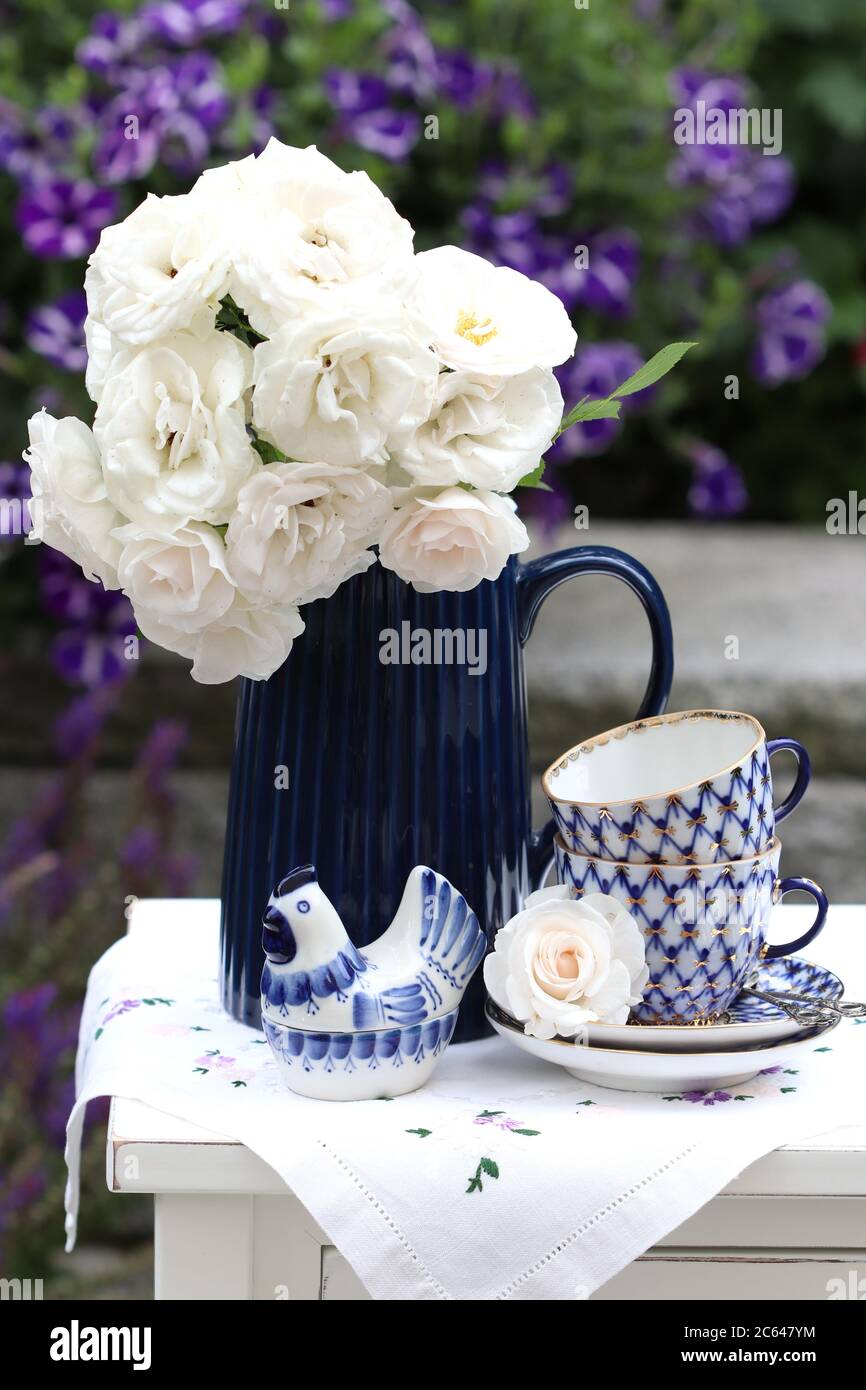 Blumenstrauß aus weißen Rosen in Vase und Vintage Kaffeetassen als Sommerdekoration Stockfoto