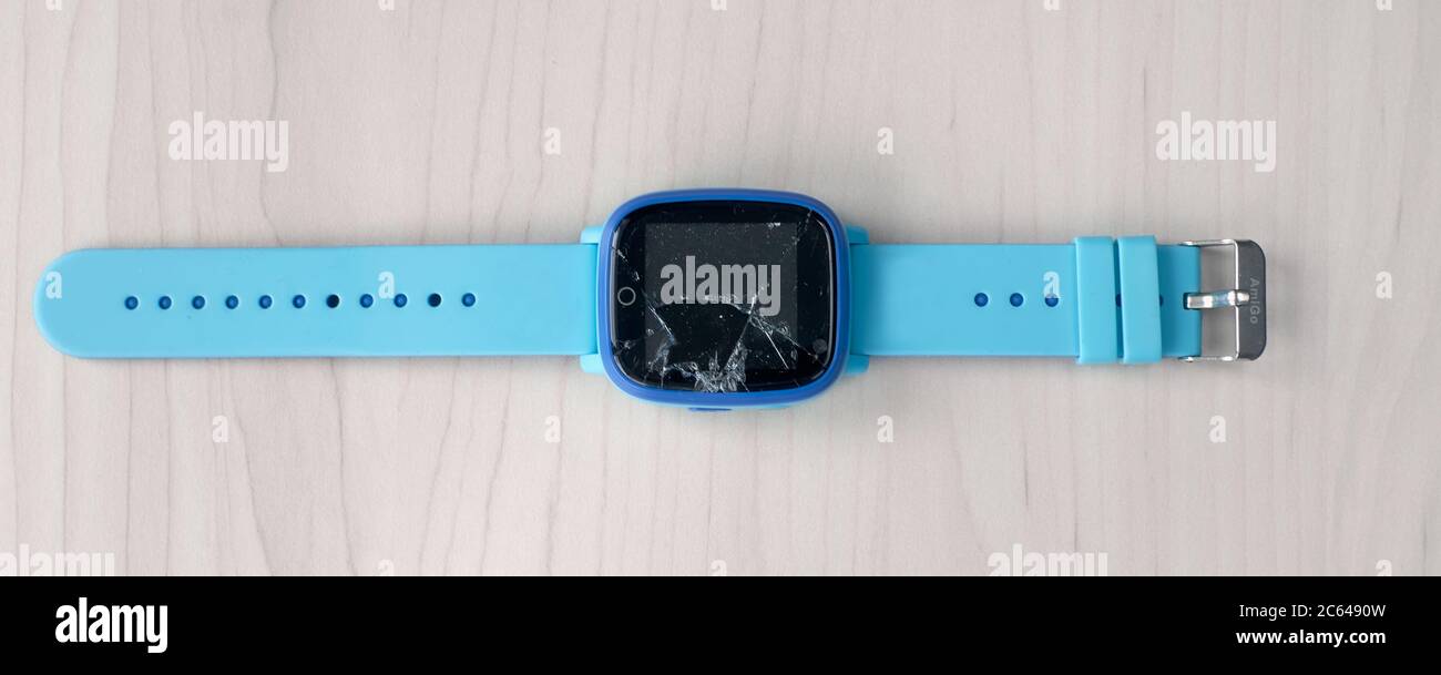 Bunte Kinder Smart Watch Telefon mit kaputtem Bildschirm auf einem hellen Holztisch. Technologie für Kinder. Tragbares Gadget-Konzept. Draufsicht, Nahaufnahme Stockfoto