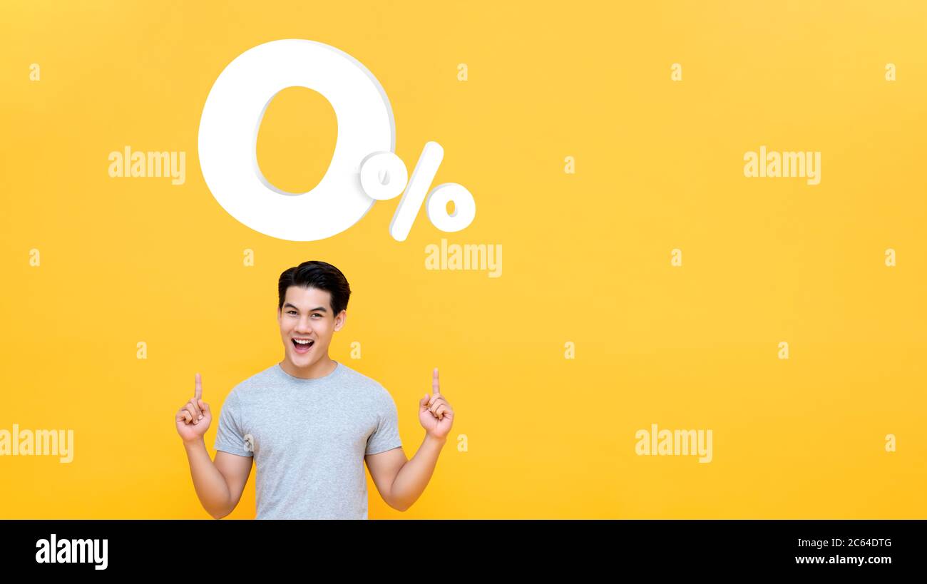 Junge gut aussehende asiatische Mann zeigt bis zu 0% auf gelbem Hintergrund mit Kopieplatz für keine Zinsen Ratenzahlung Konzept Stockfoto