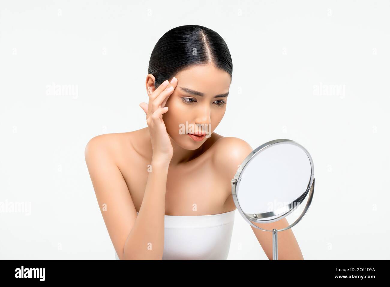 Junge schöne asiatische Frau suchen in den Spiegel und berühren ihr Gesicht, um Falten auf weißem Hintergrund für Hautpflege und Schönheit concep isoliert überprüfen Stockfoto