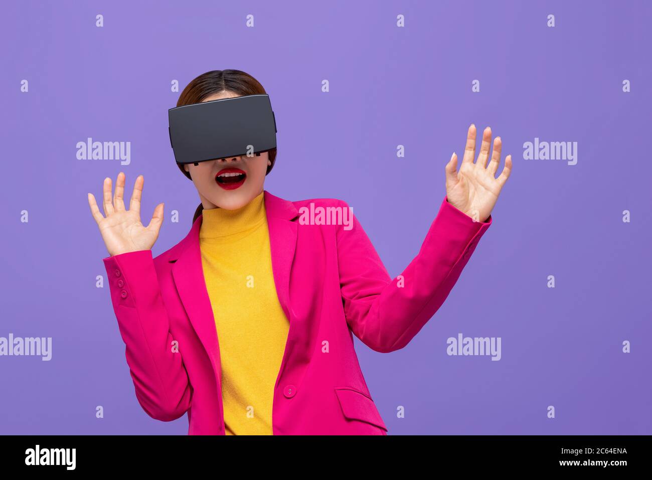 Schockierte Frau in bunten Kleidung beobachten 3D-Simulation Video aus der virtuellen Realität oder VR-Brille auf lila Hintergrund Stockfoto